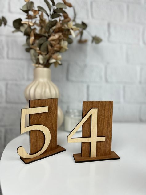 For a charming touch to your wedding reception, consider incorporating rustic wood table numbers into your wedding table decor. These beautifully crafted table numbers not only add a touch of natural elegance but also help guests easily locate their designated tables. Pair them with a matching wedding table sign or table seating sign for a cohesive look that enhances the overall ambiance of your celebration. Either nestled among floral centerpieces or placed atop crisp linens, these wedding tabl Western Table Numbers, Wood Wedding Signage, Table Seating Sign, Wedding Table Decor Rustic, Table Numbers Wood, Rustic Wedding Table Numbers, Table Number Ideas, Wood Table Numbers Wedding, Rustic Wood Table