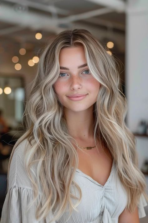 Woman with long blonde wavy hair and a necklace smiling indoors with blurred lights in the background. Blonde Balayage Light Skin, Blonde Highlight Shadow Root, Blond Hair Highlights And Lowlights, Hombre Blonde Hair, Soft Summer Balayage, Pale Blonde Balayage, Teddy Blonde Balayage, Coconut Cream Blonde Hair, Fall Hair Inspo For Blondes