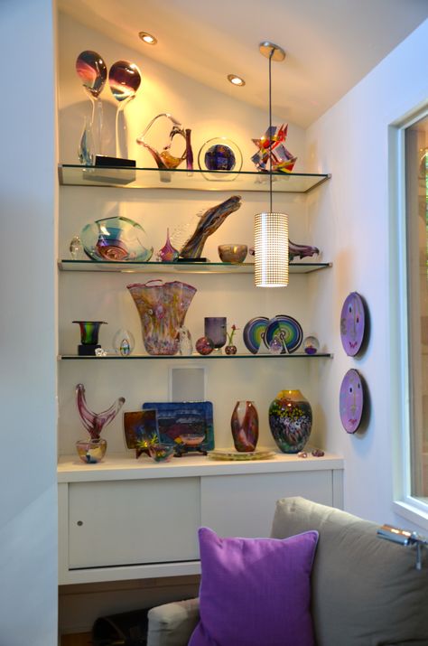 We created floating glass shelves in the niche beside a fireplace to showcase a client's glass art. The shelves are weighted at the bottom with a floating cabinet to house electronics and the space left underneath is perfect for a container of fire wood. Mirrored Shelves Floating, Decorating Glass Shelves In Living Room, Showpiece Shelves, Purse Closet, Floating Cabinet, Glass Shelves Decor, Recessed Shelves, Shelves Decor, Floating Glass Shelves