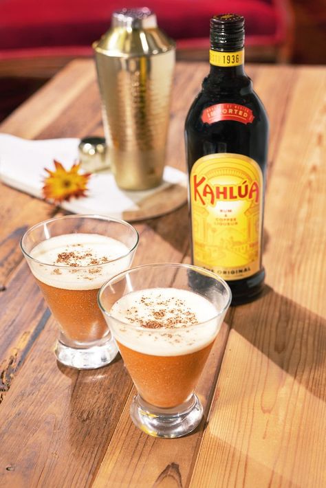 Two Pumpkin Spice Martinis sit on a wooden table with a bottle of Kahlúa coffee liqueur just behind. In the background stands a metal cocktail shaker on top of a napkin, with a brown leaf next to it. Pumpkin Martini Recipe, Pumpkin Spice Martini, Kahlua Drinks, Pumpkin Martini, Pumpkin Spice Latte Recipe, Classic Drinks, Espresso Martini Recipe, Booze Drink, Pumpkin Syrup