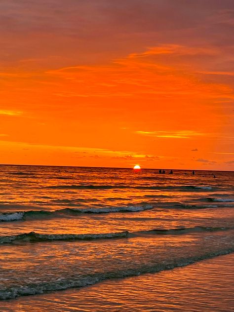 A view of the sunset at the shore from the beach. The sky is a bright orange with half of the sun still shining. Soft waves are flowing onto the shore. The waves have a bit of the orange reflected onto them from the sunset. Orange Ocean Aesthetic, Golden Hour At The Beach, Orange Beach Aesthetic, Orange Sunset Beach, Ocean At Sunset, Pretty Sunsets, Sunrise Orange, Ocean Surf, Orange Sunset