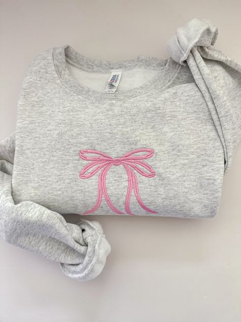 Stay chic in this minimal embroidered bow crewneck! Embroidered on a cotton blend sweatshirt, this minimal, dainty design is sure to go with any cute outfit! Embroidery Items To Sell, Boutique Sweatshirts, Coquette Gifts, Cute Crewneck Sweatshirt, Bow Sweatshirt, Embroidered Bow, Ribbon Gift, Bow Ribbon, Cute Preppy Outfits