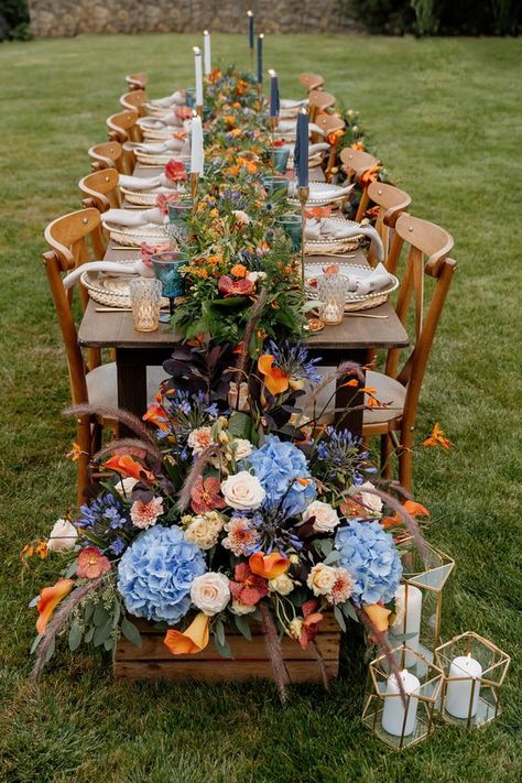 Cornflower blue and orange for fall wedding colors 2025, cornflower blue bridesmaid dresses, white bridal gown, navy blue groom suit, cornflower blue and orange flowers of boutonniere and centerpieces, white wedding cake with orange flowers décor. Orange And Blue Tablescape, Fall Wedding Color Schemes Blue, Blue And Orange Wedding Centerpieces, Blue And Orange Spring Wedding, Blue And Orange Fall Wedding, Blue And Orange Wedding Flowers, Wedding Cake With Orange Flowers, Cake With Orange Flowers, Orange Spring Wedding