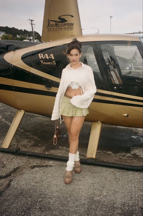 girl standing in front of a helicopter wearing a school girl outfit. Small sweater over a collared button up with leg warmers and brown loafers with a mini Louis Vuitton bag Loafer Mini Skirt Outfit, Loafer Leg Warmer Outfit, Mini Skirt Leg Warmer Outfit, Loafers And Leg Warmers, Platform Loafers Outfit, Louis Vuitton Mini Bag, Leg Warmer Outfit, Funky Fits, Loafers Outfit