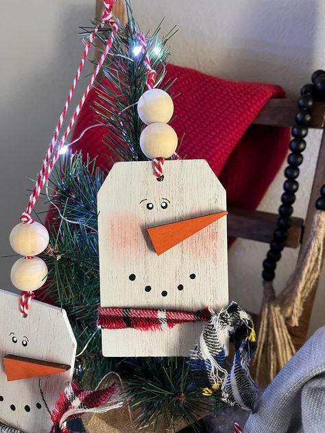 ONE Snowman wooden tag! These ornamnet/tags  are made from wood, hand painted  by me, and embellished with a flannel scarf and hangs from a jute string with 2 wooden beads. Use these in your tiered tray decor, hang from your tree, tie on a package, use as a placemarker or tuck into your tray and add a bit of whimsy. Handmade Smoke free home Listing is for ONE tag Approx. 7x2.5 from top to bottom including string hanger ** other items may be purchased in separate listings** Small Wood Circle Craft Ideas, Christmas Tag Ornaments Diy, Small Wooden Christmas Crafts, Wood Tags Christmas, Wood Biscuit Christmas Tree, Wooden Tags Ideas Diy Christmas, Wooden Christmas Gift Tags, Wood Tag Ornaments, Christmas Diys To Make And Sell