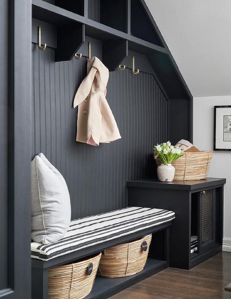 A black beadboard backsplash fitted with brass hooks mounted under black overhead shelves accents a black built-in mudroom bench topped with a black striped cushion. Black Beadboard Backsplash, Black Beadboard, Overhead Shelves, Amy Berry, Transitional Laundry Room, Black Bench, Beadboard Backsplash, Mudroom Design, Brass Hooks