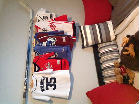 A cool way to display my son's jerseys (using his Opa's old hockey stick from the NHL) Girls Hockey Bedroom, Ice Hockey Room, Hockey Jersey Display, Hockey Room Decor, Jersey Hanger, Room Flags, Hockey Bedroom, Hockey Room, Hockey Decor