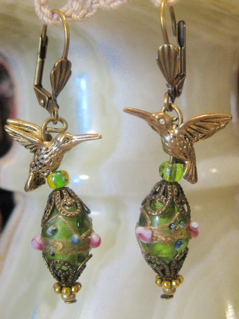 As delicate an earring as this exquisite little bird represents, gold hummingbirds meet up with lime green lamp work beads, and Czech glass beads.  These intricately crafted lamp work beads are hand blown, and are caught between antique finished brass bead caps and spacers.  All are suspended from nickel and lead free lever back wires!! So comfortable!! They measure 2 1/4 inches from the ear, and 1 1/4 inches from the wire. FREE gift wrapping upon request!! Lampwork Bead Earrings, Hummingbird Earrings, Green Lamp, Beaded Earrings Diy, Humming Bird, Bird Earrings, Earrings Inspiration, Little Bird, Hummingbirds