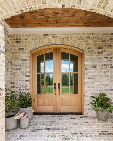 A grand entrance begins with a beautiful front door. This stunning arched double door, stained to match the rich wood ceiling of the front porch, sets the tone for the entire home. It’s the perfect blend of elegance and warmth, welcoming guests with style from the very first step. Arch Front Door Exterior Farmhouse, Arch Front Porch Entrance, Round Double Door, Staircase By Front Door, Rounded Front Door Entrance, Arched Wood Front Door, Arched Double Front Doors, House Doors Front Entrance, Curved Front Door