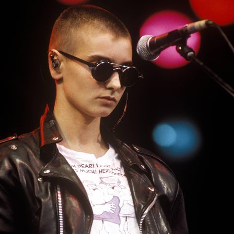 In 1990, Sinéad O'Connor headlined Glastonbury wearing a leather jacket, a “Fat Slags” tee tucked into her jeans, and round sunglasses. It's Noah Johnson's favorite look from the Irish superstar, but he'll never attempt to recreate it. Lesbian Clothes, Shave Head, Irish Singers, Oufits Casual, Bald Women, Shaved Head, Estilo Punk, Badass Women, Iconic Women