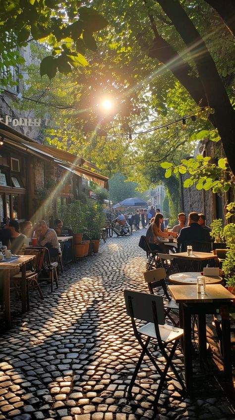 Sunlit Cobblestone Alley: A serene sunlit alleyway with people enjoying outdoor dining on a beautiful cobblestone street. #sunlight #alley #cobblestone #dining #outdoor #trees #city #cafes #aiart #aiphoto #stockcake https://ayr.app/l/ic7K City Trees Street, Italian Cobblestone Street, Parisian Patio, Exterior Reference, Urban Hiking, Candela Obscura, Streetscape Design, Pretty City, Cobblestone Street