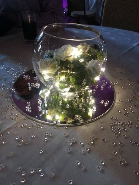 6 inch fishbowl centrepiece on mirror plate with white silk rose ivy and purple lights. Mirror Plate Centerpiece, Shire Decor, Fishbowl Decor, Prom Centerpieces, Fishbowl Centerpiece, Geometric Terrarium Wedding, Mirror Centerpiece, Terrarium Centerpiece, Terrarium Wedding