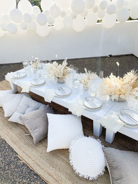 dried floral centerpiece, modern boho picnic design, fringe napkin, neutral tone table design, white stacked plates, low table design, los angeles wedding planner, los angeles event planner, rooftop dinner party, pillow floor seating, balloon decor installation Low Picnic Table Ideas, Floor Party Seating, Pillow Table Party, Pillow Seating Floor Party, White Picnic Table Decor, All White Picnic Decor, White Picnic Ideas, Low Picnic Table Outdoor Parties, Floor Table Seating Party