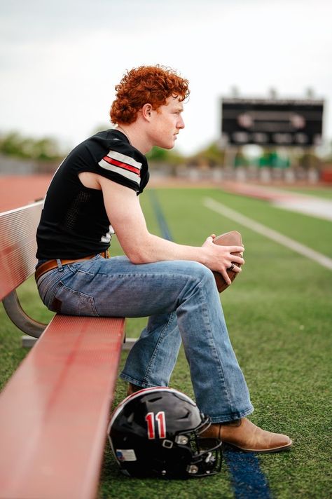 high school senior boy poses on red bench on sideline of football field holding football in hands, elbows on legs, looking out at the 50 yard line. He has red curly hair, a football jersey, blue jeans, and cowboy boots. A helmet sits on the ground and the scoreboard is in the background. Football Senior Photos, Football Senior Pictures, Boy Senior Portraits, Senior Photos Boys, Football Poses, Senior Football, Male Senior Pictures, Football Photography, High School Senior Pictures