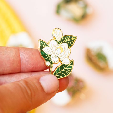 How beautiful are the white, creamy petals of the magnolia flower? Surprisingly, these delicate looking blossoms are actually HUGE, and can be up to one foot in diameter! Luckily, this pin version is much smaller, so that you can easily pin it on your jacket or bag. An enamel pin to add flair to your collar, jacket, or bag. Perfect for collecting, displaying, or gifting to a friend! The pin is made with hard enamel and polished gold-colored metal plating. It has two posts on the back for extra s Charm Casting, Plant Enamel Pin, Enamel Pin Display, Southern Magnolia, Enamel Pin Collection, Lapel Pins Mens, Pretty Pins, Magnolia Flower, Cool Pins