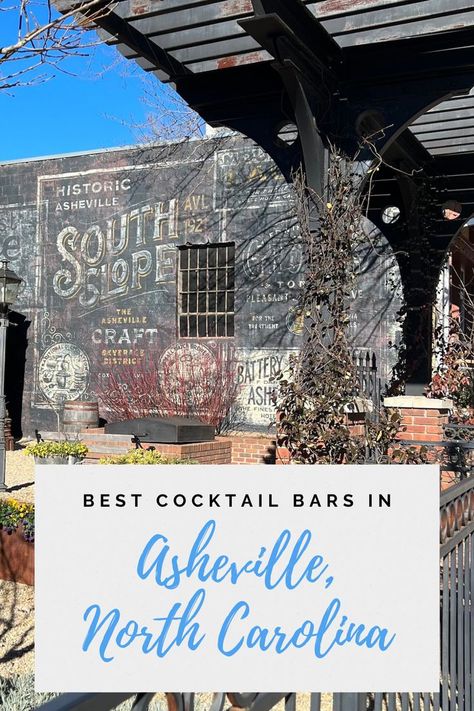 a photo of the outside patio of The Chemist on South Slope in Asheville, NC. There is a corner of blue sky in the top left. Below that is a wall of a building that has a black mural on it with white and yellow letters that say Historic Asheville South Slope, the Asheville Craft Beverage District. Visit North Carolina, North Carolina Vacations, Best Cocktail Bars, Western Nc, Cocktail Bars, Biltmore Estate, Asheville North Carolina, Anniversary Trips, Places Of Interest