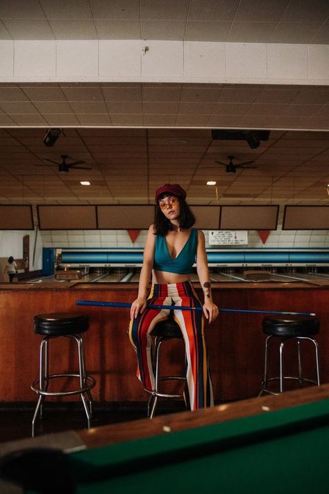 Model sits on a stool with a billiards cue lain across her lap. Retro Bowling Alley Photoshoot, Bowling Alley Photoshoot, Alley Photoshoot, Billiards Aesthetic, Posing Photography, Ig Model, 70’s Fashion, Bowling Alley, Photoshoot Themes