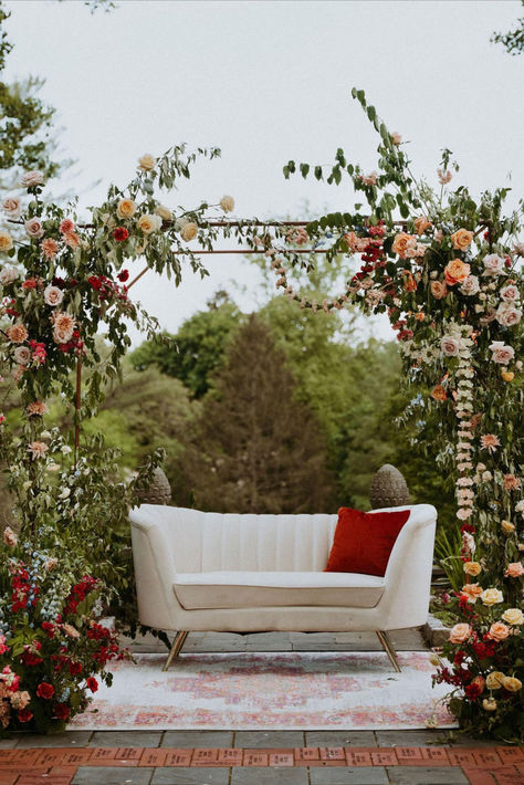 White sofa with red pillow under canopy of florals in the garden at Gramercy Mansion, one of the best historic wedding venues in Baltimore. Floral Arrangement Wedding, Indoor Wedding Reception, Wedding Floral Arrangement, Floral Ceremony, Tablescape Wedding, Floral Archway, Indoor Wedding Receptions, Corporate Event Planner, Secret Garden Wedding