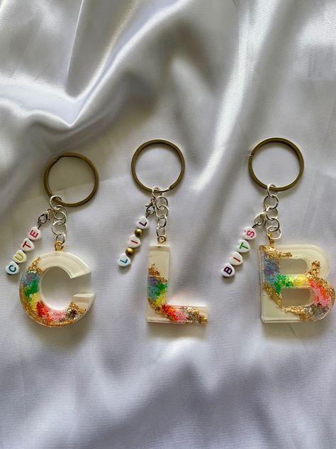 This  is a resin keychain, with a rainbow geode design, made from star shaped iridescent/opal glitter, on a white background. Keychain includes a custom name charm, made with rainbow colour letter beads. Rainbow Resin Keychain, Glitter Resin Keychain, Name Resin Keychain, Resin Letter Keychain Ideas, Resin Name Keychain, Letter Resin Keychain, White Glitter Background, Rainbow Geode, Resin Letter Keychain