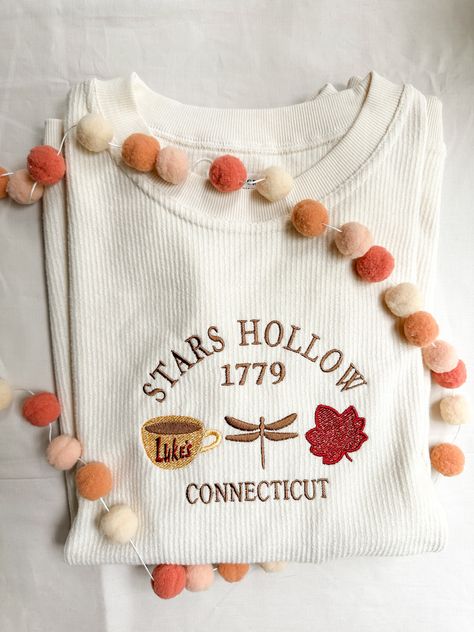 Details Step into the cozy charm of Stars Hollow with our Gilmore Girls-inspired corded crew embroidered pullover! Featuring a soft cream color and intricate embroidery, this pullover celebrates all things Stars Hollow, Connecticut, including Luke’s Diner, a dragonfly, and a signature autumn leaf. Crafted with high-quality stitching, it's the perfect gift for any Gilmore Girls fan or someone looking to channel their inner Lorelai. Whether you're sipping coffee at Luke's or strolling the town squ Stars Hallow Christmas, Fall In Stars Hollow, Stars Hollow Crewneck, Stars Hollow Fall, Towns Like Stars Hollow, Embroidered Pullover, Gilmore Girls Fan, Sipping Coffee, Fall Dog