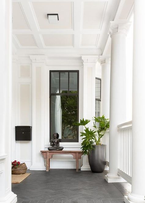 Transitional porch with dark gray herringbone pattern floor pavers furnished with a chinoiserie bench under a window beside a tall black planter. Front Door Bench, House Ideas 2023, Front Porch Stone, Global Interior Design, Porch Walkway, Patio Refresh, White Rocking Chairs, Door Bench, Front Door Lighting