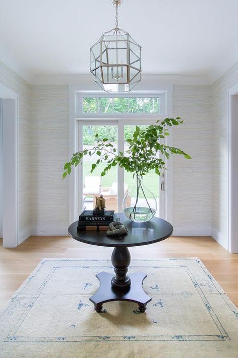 A Suzanne Kasler Morris Lantern hangs over a round black accent table placed in an entry on an ivory and blue rug. Round Foyer Table Decor, Round Entryway Table, Entryway Round Table, Black Entry Table, Round Entryway, Foyer Table Decor, Round Foyer Table, Round Entry Table, Entryway Table Ideas