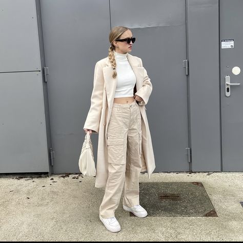 girl standing in front of a grey building wearing beige cargo pants, a white turtleneck, a beige oversized coat, a beige handbag and brown sunglasses How To Style Cream Cargo Pants, Chic Cargo Pants Outfit, Beige Cargo Pants Outfit Winter, Outfit Cargo Beige, Style White Cargo Pants, Cargo Pants Outfit Aesthetic, Cargo Pants Outfit Winter, Beige Cargo Pants Outfit, Fashion Trends Aesthetic