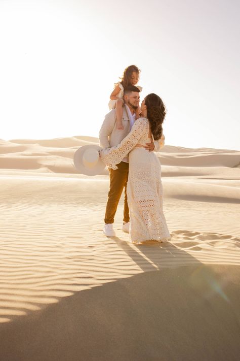 A husband and wife stand face to face while the father carries heir young daughter on his shoulders surrounded by endless sand dunes. Sand Dune Family Photos, Dunes Family Photoshoot, Sand Dunes Photoshoot Family, Family Dunes Photoshoot, Sand Dunes Outfit, Sand Dune Maternity Photos, San Dunes Maternity Photoshoot, Sand Dunes Couple Photoshoot, Wedding Pictures Beach