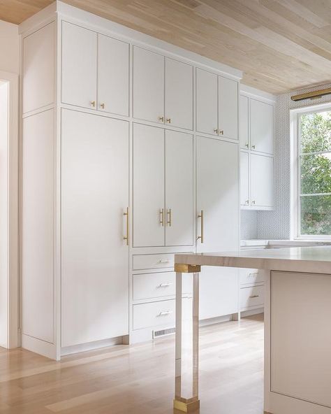 Brass and lucite legs, placed on gray wash wood floors under an oak plank ceiling, accent a white island topped with a gray and white marble countertop facing white concealed fridges placed both under and on either side of white flat front cabinets adorning Lewis Dolan Bar Pulls and Knobs. Kitchen Cabinets Pulls And Knobs, Cabinets Pulls And Knobs, Kitchen Cabinets Pulls, Flat Panel Kitchen Cabinets, Inset Kitchen Cabinets, Flat Front Cabinets, Flat Cabinets, Slab Cabinets, Inset Cabinets