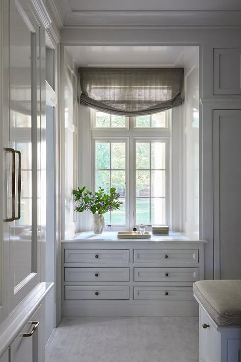 Chic walk in closet features a white built in dresser with brass knobs under a window with tan shade. Walk In Closet With Window Ideas, Built In With Slanted Ceiling, Pass Through Closet To Bathroom, Window In Walk In Closet, Built In Dresser Under Window, Window In Master Closet, Closets With Windows, Built In Wardrobe Around Window, Closet Designs With Window