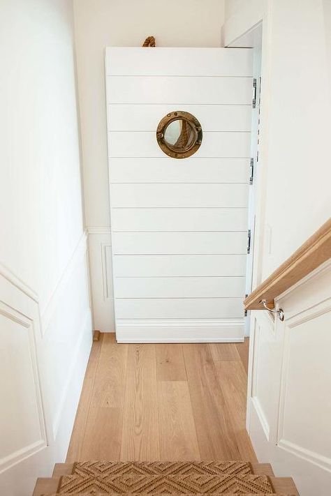 Cottage foyer boasts an interior staircase fitted with a jute diamond pattern runner along with a door showcasing a wood porthole. Beach House Staircase, Cottage Foyer, Shiplap Door, Outdoor Bar And Grill, River House Decor, Chicago Interior Design, Zen House, Bunk Beds Built In, Interior Staircase