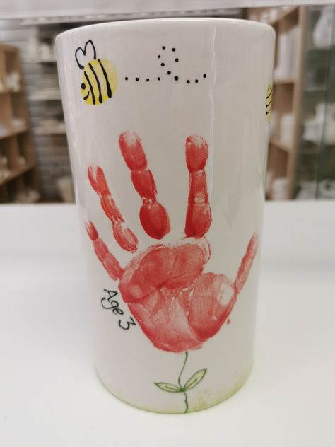 Handprint flowers and fingerprint bees on vases still continue to be popular, this young man came with his 'enthusiastic nanny' - her words not ours to make this for his mummy and daddy! #handprintflower #vase #paintyourown #fingerprints #bees Handprint Vase Craft, Handprint Mug Diy Mother's Day, Color Me Mine Mothers Day, Hand Print Flower Bouquet, Hand Print Mug, Pottery Painting Handprint Ideas, Hand Print Pottery Ideas, Handprint Pottery Ideas, Handprint Coffee Mug