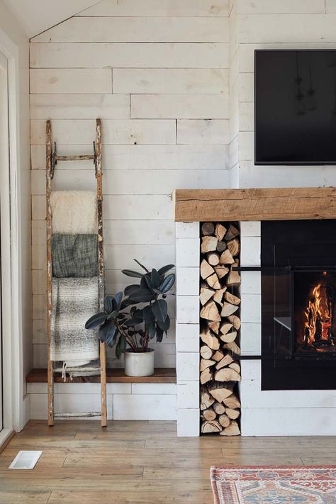 Revamp your fireplace mantel with a farmhouse-inspired look like this one in Kate and Tony Becker’s Corcoran home. Using barn wood adds character and charm, while throwing a blanket ladder, shiplap panels, and built-in firewood holder into the mix ties a simple, stylish aesthetic into your home. Photo by Wing Ta. Fireplace With Space For Wood, Wood Holder In Fireplace, Blanket Ladder Fireplace, Blanket Ladder Next To Fireplace, Wood Holders For Fireplace, Fireplace Blanket Ladder, Wood By Fireplace, Blanket Ladder By Fireplace, Firewood Storage Built In Fireplace