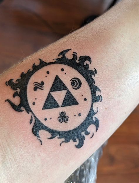 Tattoo on forearm of symbols from the Legend of Zelda video game. Comprises 3 triangles to make one bigger one surrounded by a ring of cartoon fire and thre other symbols representing other elements in the game. Zelda Ocarina Of Time Tattoo, Ocarina Tattoo, Legend Of Zelda Tattoo Ideas, Ocarina Of Time Tattoo, Zelda Tattoo Ideas, Legend Of Zelda Tattoo, 23 Tattoo, Brothers Tattoo, Video Game Tattoos