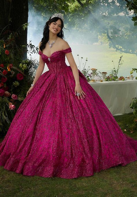 Embrace the magic of your quinceaera in this enchanting Vizcaya ball gown (style 89455). The off-the-shoulder bodice is crafted from a subtly sheer fabric, offering a touch of ethereal beauty. The bust is delicately draped, highlighting your unique silhouette, while peek-a-boo jewel beading adorns the lovely sweetheart neckline, adding a touch of sparkle.The real magic unfolds in the skirt, made from intricately patterned glitter tulle. This luxurious fabric boasts an unreal sparkle that will catch the light with every move. A beautiful brooch adorns the center of the bodice, further enhancing your radiant shine. To add a touch of drama and whimsy, the dress features an oversized, detachable back bow. This allows you to personalize your look and create a truly unforgettable entrance.To com Magenta Ball Gown, Magenta Quinceanera Dresses, Quincenera Dresses, Sheer Corset, Jewel Encrusted, Quince Dress, Princess Sleeves, Terani Couture, Charm School