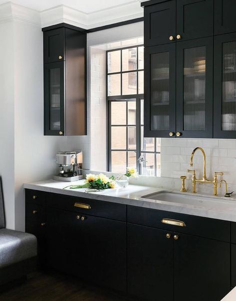 Black kitchen features glass reeded upper cabinets and black lower cabinets adorned with polished brass hardware paired with white marble countertops and a white subway tile backsplash. Black Kitchen, Black Cabinets, Counter Tops, A Kitchen, Kitchen Decor, Kitchen Cabinets, Handles, Marble, Brass