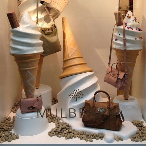 This window display shows lighting, props, and color/texture. The warm lighting makes it appear like it is the cause of the ice cream melting. The giant props of melting ice cream cones and toppings adds a whimsical like display. That compared with the texture of the cones and soft serve ice cream make it seem like the props are real. The color of the bags is matched perfectly with the cones it makes perfect sense to why these props were chosen. Ice Cream Window, Summer Window Display, Window Display Retail, Summer Window, Visual Merchandising Displays, Store Window Displays, Display Props, Ice Cream Cones, Retail Store Design