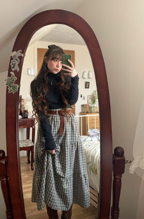 Girl with long wavy brown hair and a bow takes mirror selfie in vintage oval wooden mirror. She is wearing a three tiered dark green plaid maxi skirt with a brown buckle belt and a black long sleeve turtleneck and brown combat boots Architecture Outfit Style, Cute Cottagecore Outfits Winter, Cottage Core Womens Fashion, Easter Vigil Outfit, Winter Outfit Cottagecore, Cottagecore Outfits Work, Cute Winter Skirts, Style Long Skirt Winter, Cozy Cottage Core Outfit