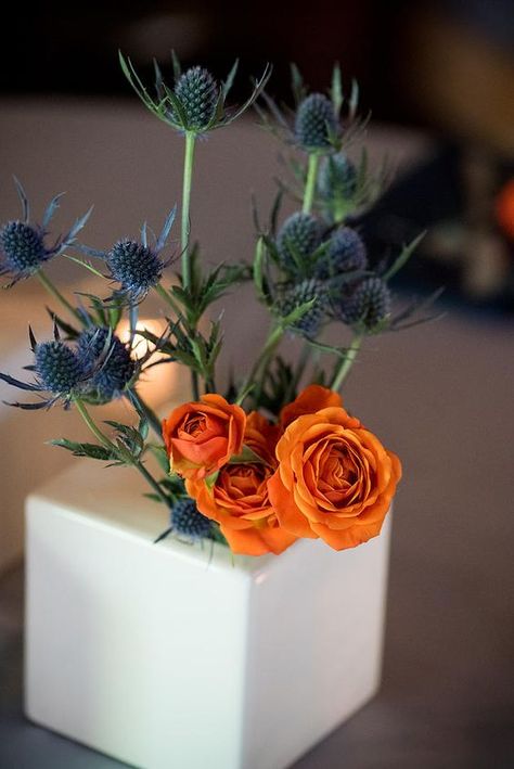 Orange Blue Floral Arrangements, Orange Flower Centerpieces Simple, Blue And Orange Event Decor, Blue And Orange Centerpieces Wedding, Orange Rose Centerpiece, Green And Orange Centerpieces, Blue Orange Flower Arrangements, Orange Blue Flower Arrangement, Orange And Blue Floral Arrangements