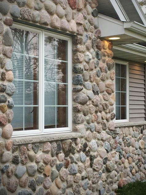 Granite veneer stone home shows Buechel Stone Granite Cobbles stone facade exterior stone veneer with siding. This residential natural stone install is in a fieldstone mosaic real stone pattern using mortar masonry (vs dry stacked stone) for a classic rustic cobbles look. See stone masonry blog post (https://www.buechelstone.com/masonry/) for more details on how to install stone veneer. #StoneVeneer #Fieldstone #StoneHome #StoneFacade #StoneCladding #ExteriorStoneVeneer #Masonry #GraniteVeneer Stone Facade House Exterior, Stone Facade Design, House Facade Design, Wall Veneer, Exterior Stone Veneer, Stone Siding Exterior, Buechel Stone, Home Facade, Stone Veneer Exterior