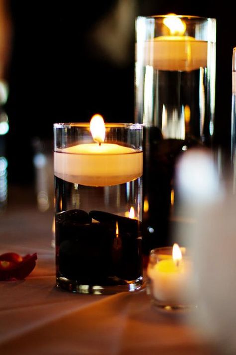 centerpiece with rocks and floating candle Black Floating Candle Centerpieces, Black White And Blus Centerpiece With Floating Candles And Flower Ring, Black Floating Candles, Floating Candle Centerpieces Black Tablecloth, Black Vase Centerpiece, Floating Candle Centerpueces, Roses In Water Centerpiece Floating Candles, Cylinder Centerpieces, Black River Rock