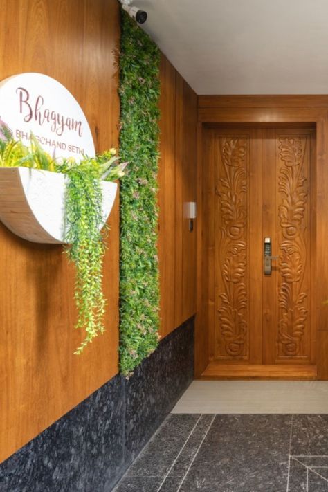 The main door exhibits grandeur in its natural wood carving. A nameplate bearing the words ‘BHAGYAM’ rests on the teak wood paneling used in the entrance Flat Entrance Lobby Design, Flat Entrance Design, Lobby Design Ideas, Entrance Lobby Design, Cool Interior Design, House Entrance Doors, Minimal Interiors, Cool Interior, Luxurious Apartment