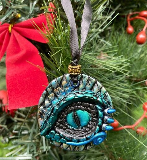 "Searching for a one-of-a-kind gift for a medieval fantasy lover? Look no further. This handmade polymer clay Dragon eye ornament captures the essence of fantasy and brings it to life, making it an unforgettable and cherished holiday decoration adding a unique finishing touch to a fantasy-themed Christmas tree. Hand sculpted with polymer clay, this holiday tree decor is hand painted with green, gold and blue metallic pigments to bring vibrant color and highlight the scaly texture of the piece. T Dragon Christmas Ornament, Dragon Christmas Tree, Eye Ornament, Fantasy Christmas, Dragon Ornament, Themed Christmas Tree, Polymer Clay Dragon, Dragon Tree, Witch Shop