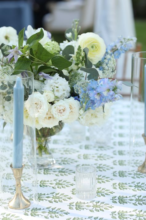 a green and white patterned table linen. the floral arrangement has white and blue flowers with greenery. Green And Blue Tablescape, Patterned Napkins Wedding, Green Wedding Linens, Blue And White Tablescapes Wedding, White Green And Blue Wedding, Wedding With Blue Accents, Blue Wedding Tablescape, Coastal Centerpiece Ideas, Summer Wedding Colors Schemes