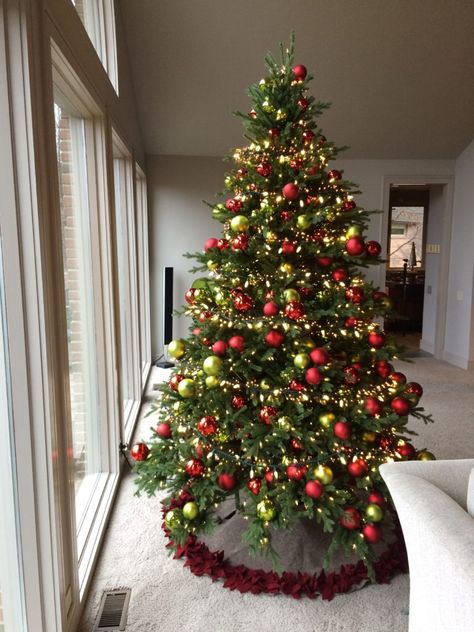 The tree is decorated with red and lime green ball ornaments, both matte and shiny, stuck with paper wrapped wire stems.  The ornaments are not hung from the tree branches in the traditional way. They are laid into and onto the tree as if they were a pick. The balls are next to weightless, so the stiff stems of the tree hold them up. Gold Red Green Christmas Tree, All Green Christmas Tree, Christmas Decorations Red And Green, Red And Green Christmas Decorations, Green Red And Gold Christmas Tree, Christmas Tree Ideas Red And Green, Red And Green Christmas Tree Decorations, Green Red Christmas Decor, Christmas Decor Ideas Red And Green