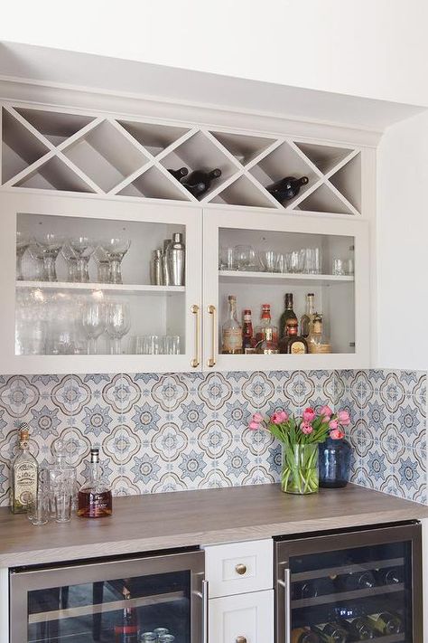 Glass built-in wine wrack above glass front cabinets accented with brass pulls in a bar nook featuring white and blue mosaic backsplash tiles. Bar Nook, Accent Tiles, Built In Wine Rack, Peony Pattern, Серая Кухня, Home Bar Rooms, Bar In Casa, Transitional Dining Room, Casa Country