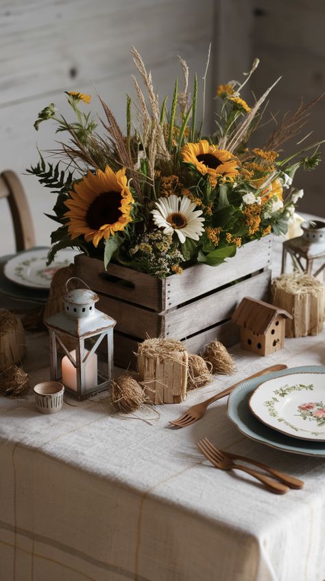 A charming farmhouse-inspired table centerpiece featuring an array of rustic elements. At the center is a wooden crate filled with freshly picked seasonal flowers, including sunflowers, daisies, and wild grasses. Check out this decorative wooden crate link in the pin. I am an affiliate marketer, so I promote products I think users will find helpful, for a commission, at no extra cost to you. Follow for more product ideas and inspiration! #decorative #farmhouse #farhmouseideas #woodencrate #DIY Rustic Farm Centerpieces, Wooden Crate Ideas, Farm Table Centerpiece, Round Table Centerpiece, Head Table Wedding Decorations, Small Wooden Crates, Garden Center Displays, Old Wooden Crates, Flowers Basket