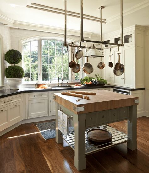 Natural light streams through the arched windows in this kitchen with white cabinetry and metal pot rack suspended over the kitchen island that sits on wide wood plank flooring. White Kitchen With Butcher Block Island, Kitchen With Butcher Block Island, Antique Kitchen Island, Butcher Block Island Kitchen, Butcher Block Island, Butcher Block Kitchen, Square Kitchen, Pot Rack Hanging, Interior Design Dining Room