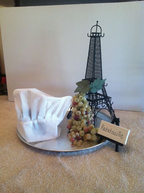 RATATOUILLE CENTERPIECE: Got the eiffel tower, the base, & the fake grapes at an Arts & Crafts Store. Got the Chef's hat from a party store. Then, I printed a picture of Remy from the Ratatouille movie, traced the image on black board, & used an exact knife to cut him out. Taped him to the inside of the hat. Added a fake tea light candle inside and turned it on during reception. Had a very tasty effect;) Ratatouille Centerpiece, Ratatouille Birthday Party, Ratatouille Movie, Pixar Party, Ratatouille Disney, Disney Movie Night, Party Drinks Alcohol, Dream Wedding Decorations, Party Invite Design