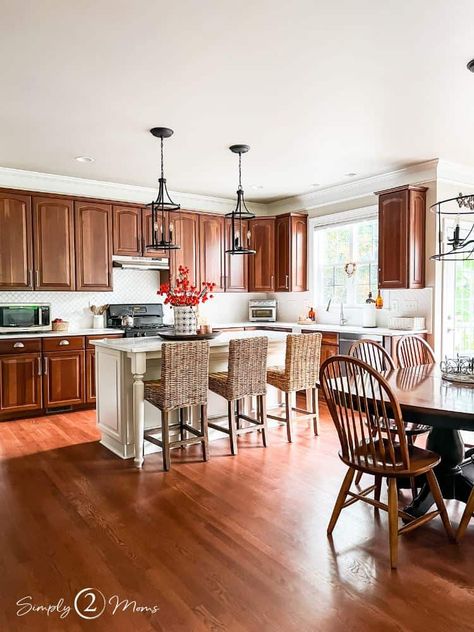 Who says a kitchen with cherry cabinets can't look modern? We've got ideas to update your kitchen with wood cabinets without painting them! This kitchen update includes a custom island with paneling and table legs. New pendant lights over the island add curves and style. Rattan counter stools add texture. White dovestone quartz counters really brighten the room. The matte white lantern tiles or arabesque tiles with white grout gives a light and bright feel. You'll love the fall decor ideas too! Cherry Cabinet Kitchen, Mahogany Kitchen Cabinets, Kitchen With Wood Cabinets, Kitchen With Cherry Cabinets, Tiny Cottage Kitchen, Mahogany Kitchen, Wicker Counter Stools, Cherry Wood Kitchen Cabinets, Cherry Wood Kitchens